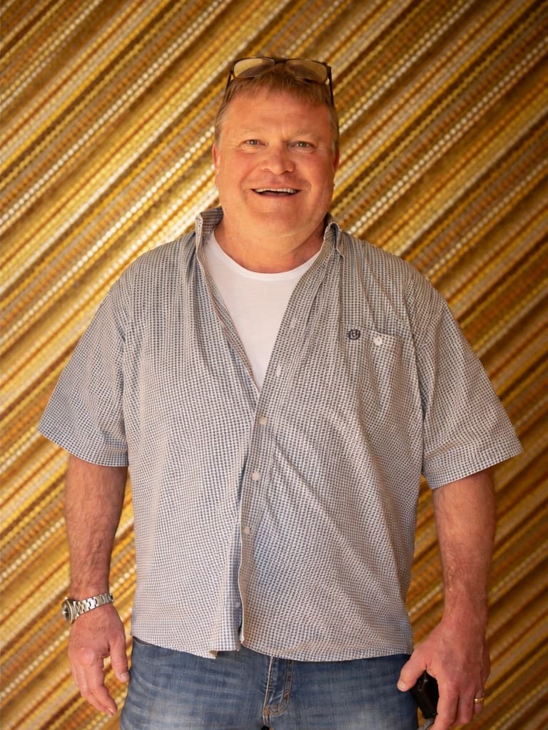 Clint Robertson smiling in a checked shirt, in front of a gold slatted wall