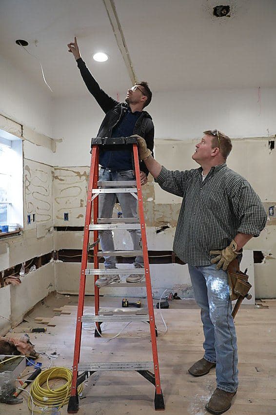 Luke Caldwell on a ladder pointing at the ceiling while Clint Robertson looks up