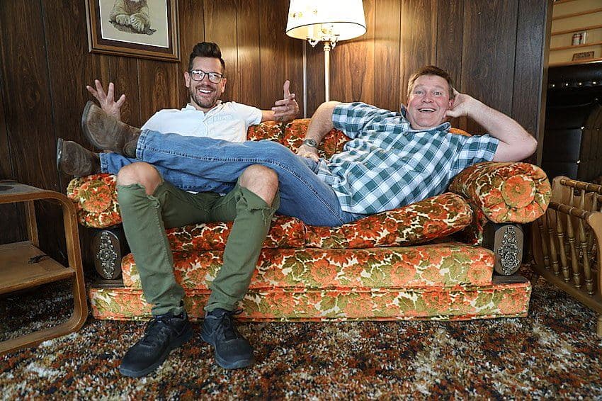 Luke Caldwell and Clint Robertson laughing on a vintage floral couch